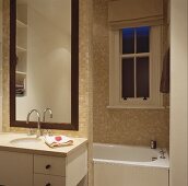 Vanity with base cabinet and drawer in front of a tall mirror on a tiled dividing wall in front of a bathtub