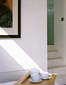 Weisses Teeservice auf Tablett neben offenem Durchgang mit gefliesten Treppenstufen