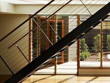 Metalltreppe mit Geländer und horizontalen Drahtseilen vor Fensterfront mit verstellbaren Glaslamellen