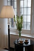 Teatime on a side table next to a floor lamp with pleated shade in front of a leaded window