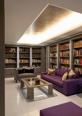 Living room with purple sofa in front of a library wall and indirect lighting under an open ceiling
