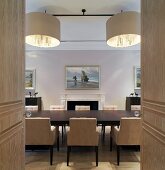 View through open double doors of dining table with upholstered chairs and designer pendant lights in dining room