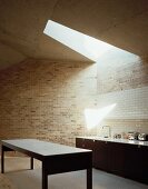 Open minimalist kitchen in front of a brick wall and skylight