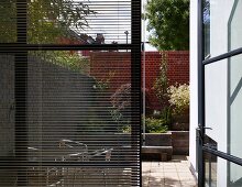 Fenster mit halbgeschlossener Jalousie und Blick durch offene Terrassentür auf Stadtgarten