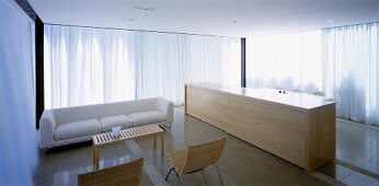 Modern living room with sofa and monolithic wooden counter in front of closed, white curtains at the window