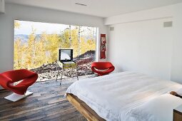 Weisses Schlafzimmer mit roten Designersesseln vor grosser Fensterfront mit Landschaftsblick