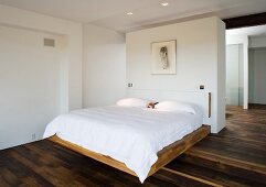 A double bed in front of a white partition wall in a bedroom with dark, rustic parquet