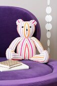 A striped teddy bear on a purple chair