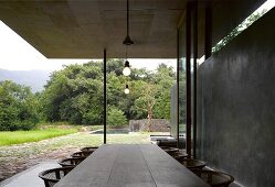 Rustikaler Tisch auf Veranda eines zeitgenössischen Wohnhauses mit Betonwand und Blick in Garten