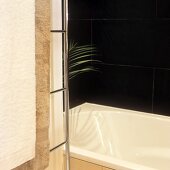 Detail of a corner of a bathroom with a bath tub and black tiles on the wall