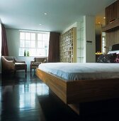 A bed with a wooden frame and an antique leather armchair in an open-plan bedroom