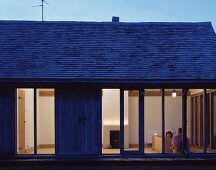 A simple detached house with terrace windows and a view into an illuminated bedroom