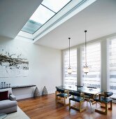 Modern living space with skylight and pendant lamps above dining table and retro leather chairs