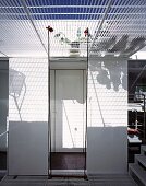 Pattern of light and shade on white wall through wire mesh floor above
