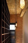 Ceiling-height, empty shelving and light bulb lamps in front of brick wall with factory window in English loft apartment