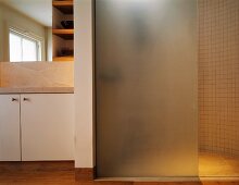 Frosted glass shower partition in bathroom with stone tiles and wooden flooring