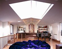 Long living room with skylight, bright blue upholstered furniture, grand piano and bar in back corner