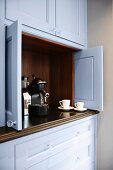 An espresso machine in a kitchen dresser with open doors