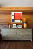 Chest of drawers with books in front of wood-panelled wall