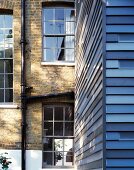 Facade with blue painted wooden slats in front of English house with brick facade