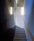 Schmaler Treppenaufgang mit schwarzen Steinfliesen an Wand und Handlauf aus Holz