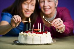 Two women lighting candles on a birthday cake