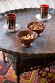 Orientalische, rote Teegläser und Schälchen mit Nüssen auf Tablett-Tisch mit Ornament