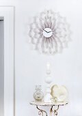 Wall clock with honeycomb frame made from strips of white corrugated cardboard above shabby chic arrangement - candles and sculptural vases on side table