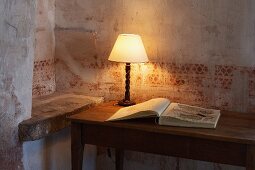 Table lamp and open book on wooden table against wall with faded stencilled pattern