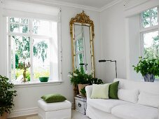 White sofa, house plants and gilt-framed, full-length mirror next to window in living room