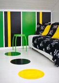 Black throw and cushions on sofa and green stool in attic room with colourful, striped wall