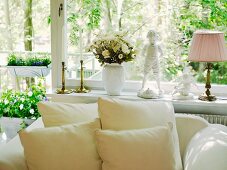 Cushions on white, upholstered armchair below large window decorated with flowers and vintage-style ornaments