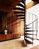 Open spiral staircase on tiled floor with sideboard in front of wood-panelled wall