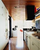 Wooden ceiling above white, fifties-style fitted kitchen