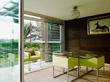 Lime-green armchairs with steel frames at glass table in dining room with view of palm trees