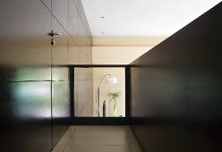 Gallery with door integrated in dark wood panelling and glass balustrade with view of living room below