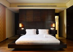 Floating double bed in front of dark wood partition