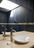 Dunkel gefliestes Badezimmer und Oberlicht im Spiegelbild über Marmorplatte mit Waschschüssel und modernem Wasserhahn