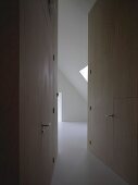 Room with sloping attic ceiling at end of narrow, tapering corridor with integrated doors flush with wood cladding