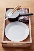 An empty place setting with a saucier in a wooden crate