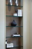 Glass shelves in niche with books and vases