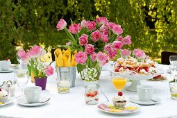 A table set for coffee in a garden with a plate of profiteroles and a vase of pink tulips