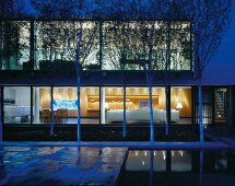 Courtyard with trees in front of contemporary house at dusk with view into illuminated interior
