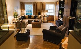 Schwarzer Polstersessel mit passendem Hocker und Sofagarnitur im klassisch modernen Wohnraum