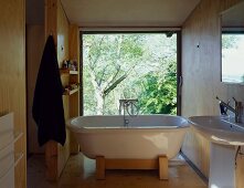 Free-standing bathtub in front of floor-to-ceiling window with view of garden