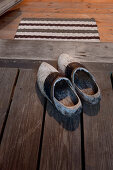 Vintage wooden clogs on board floor in front of open door with doormat