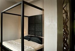 Modern canopied bed with black frame and delicately carved wooden back wall in elegant bedroom
