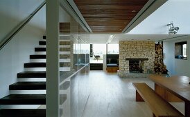 Offener Wohnraum mit Esstisch und Kamin und mit Glaswand abgetrennter Treppenaufgang