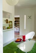 Two white, plastic shell chairs on green, flokati-style rug in open-plan interior with view of dining room