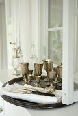 A tray of silver goblets on a white sideboard against a wall with a window